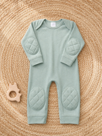 Green Tea padded onesie flat lay on woven seagrass placemat with wooden teething ring