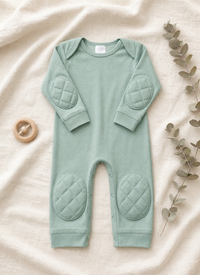 Green Tea padded onesie flat lay on cream linen with eucalyptus branch and wooden teething ring - front view