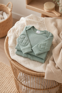 Green Tea onesie neatly folded on a rattan stool with cream knit throw - laundry day nursery styling