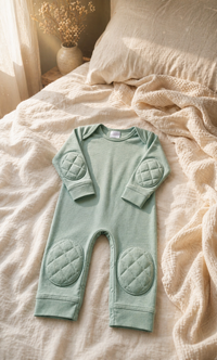 ComfyCrawlers Green Tea onesie on cream linen bedding with dried wildflowers - slow Sunday morning nursery scene