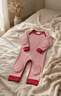 ComfyCrawlers Red Stripe onesie on cream linen bed with dried flowers in ceramic vase - warm morning nursery light